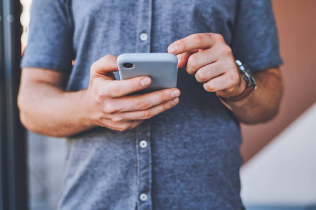Primer plano de un hombre en un teléfono navegando en las redes sociales mientras está de pie al aire libre en la calle de la ciudad. Hombre leyendo un artículo o blog en un sitio web con un smartphone en una calle urbana.